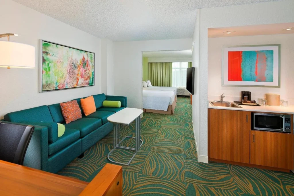Suite living area with sofa, kitchenette and two beds beyond at SpringHill Suites Marriott Village