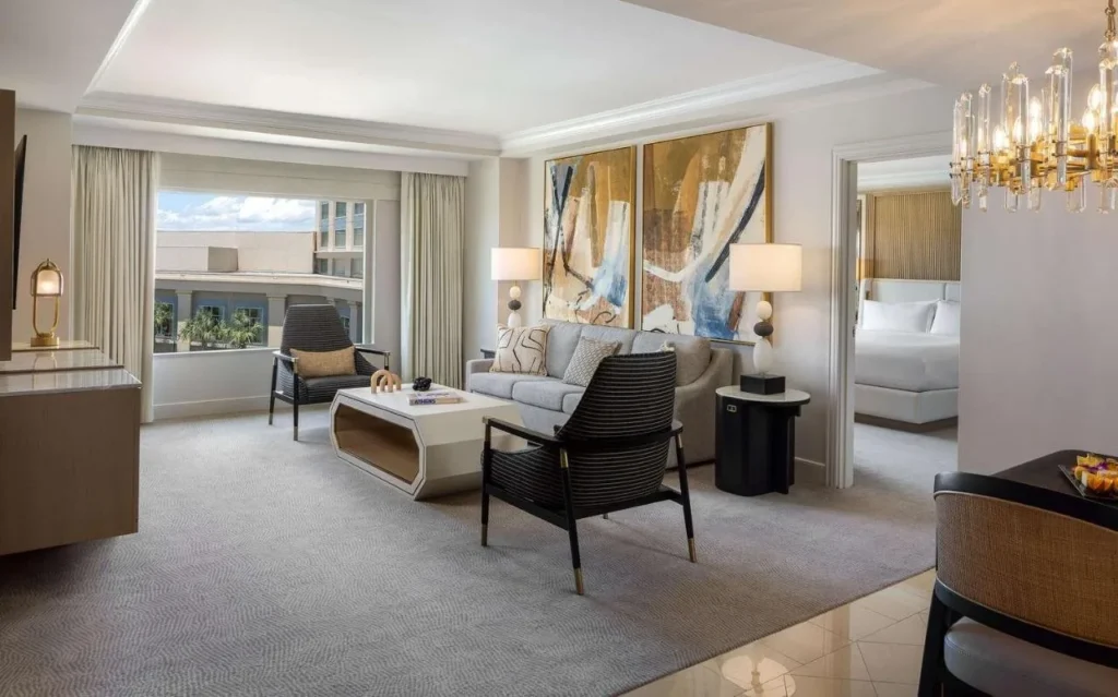 Sala de estar de la suite en Waldorf Astoria Orlando con sofá, sillones, candelabro y dormitorio más allá