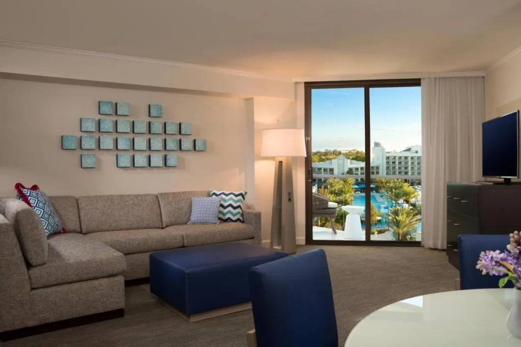 Suite living room with a sectional sofa and pool-view balcony at Hilton Buena Vista Palace