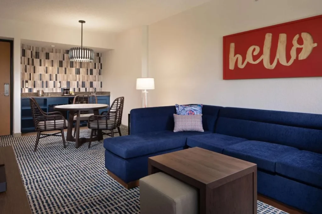 Sala de estar suite con sof&aacute; azul seccional, mesa de comedor y bar en DoubleTree Suites