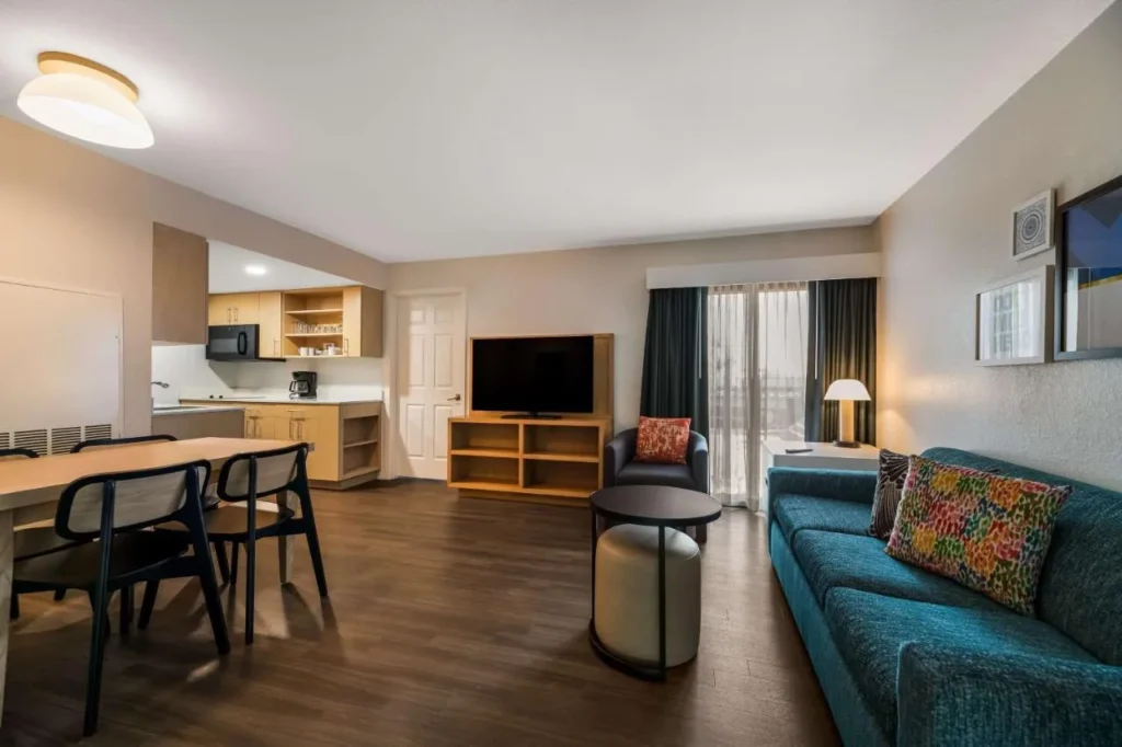 Sala de estar con sofá azul, mesa de comedor y cocina en Sonesta ES Suites Orlando