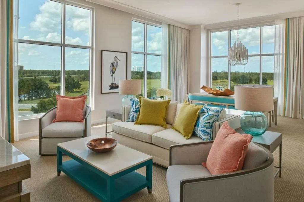 Sala de estar de la suite con coral y almohadas amarillas y ventanas altas en Gaylord Palms Resort