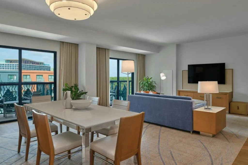 Sala de estar de la suite con mesa de comedor, sof&aacute; azul y puertas de balc&oacute;n en Walt Disney World Swan