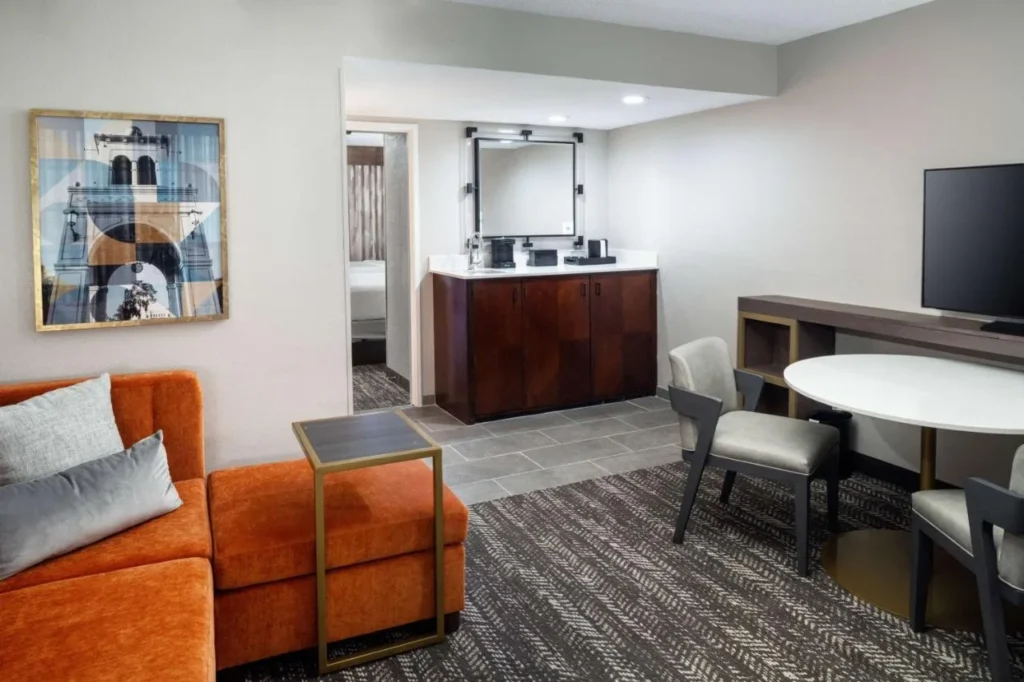 Suite living room with orange sofa, dining table and wet bar at Embassy Suites Orlando North