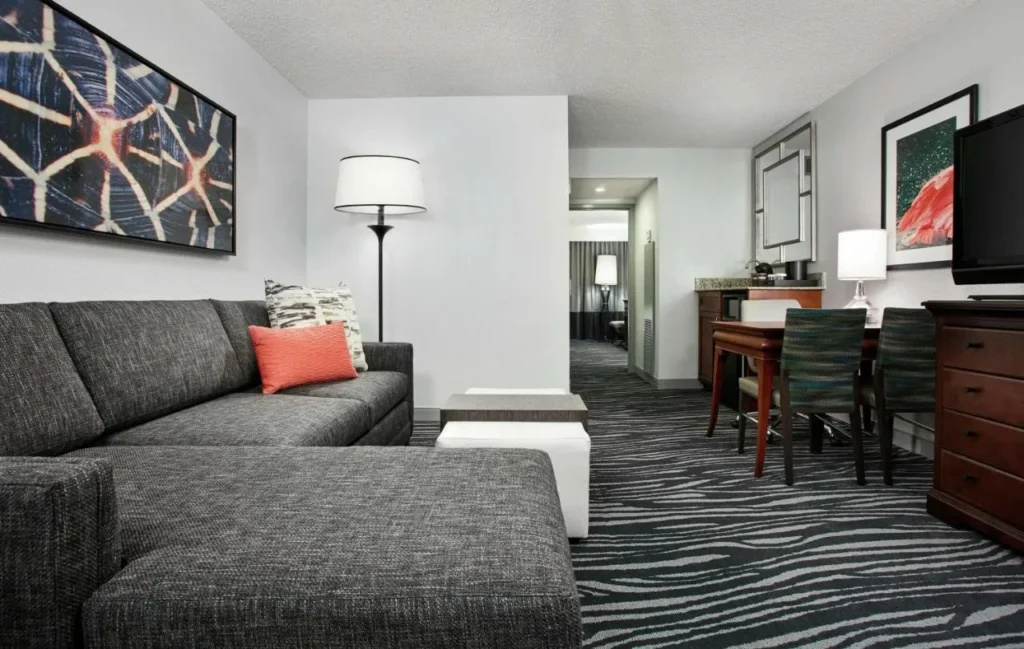 Suite living room with sectional sofa, dining table and wet bar at Embassy Suites Orlando Airport