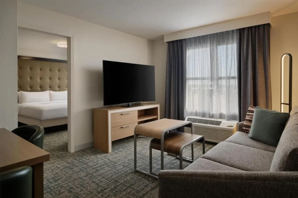 Suite con sofá y TV al lado del dormitorio en el Homewood Suites Daytona Beach Speedway-Airport