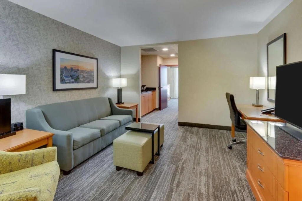 Suite living room with sofa, desk, TV and hallway at Drury Inn & Suites near Universal