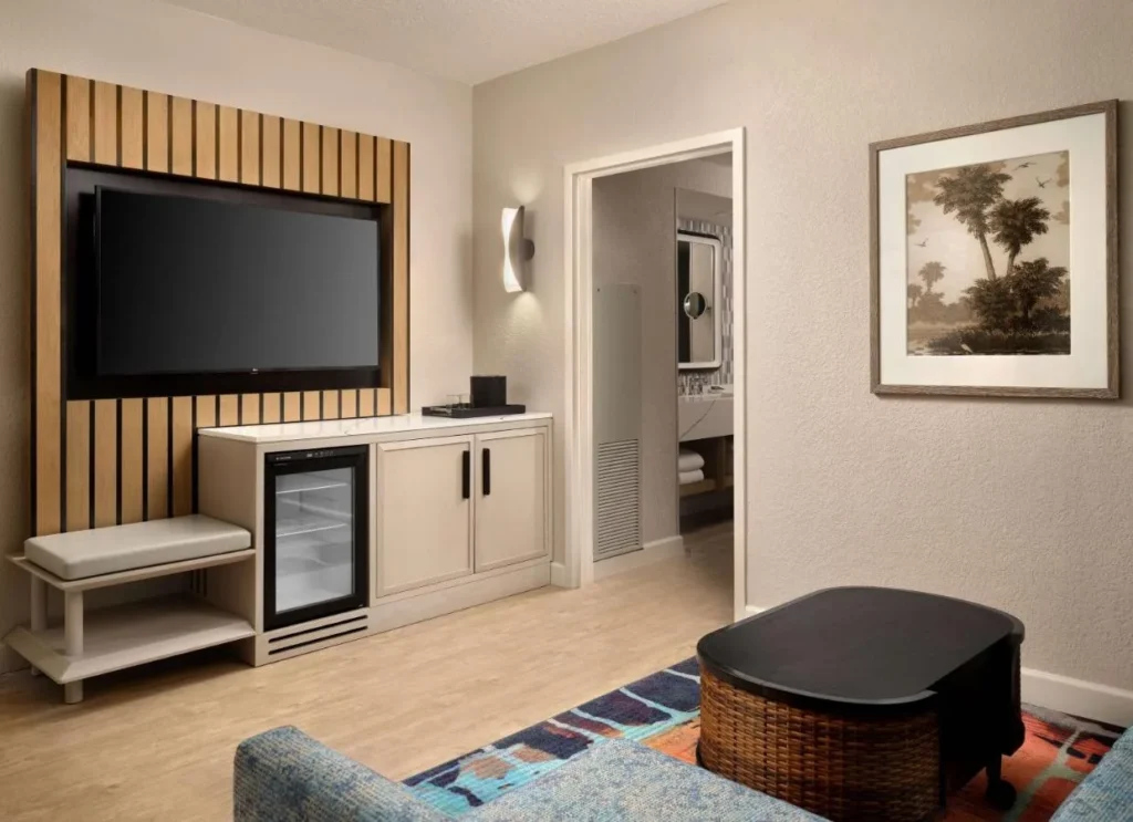 Sala de estar de la suite con TV de pared, mini refrigerador de puerta de vidrio y alfombra estampada en Caribe Royale Orlando