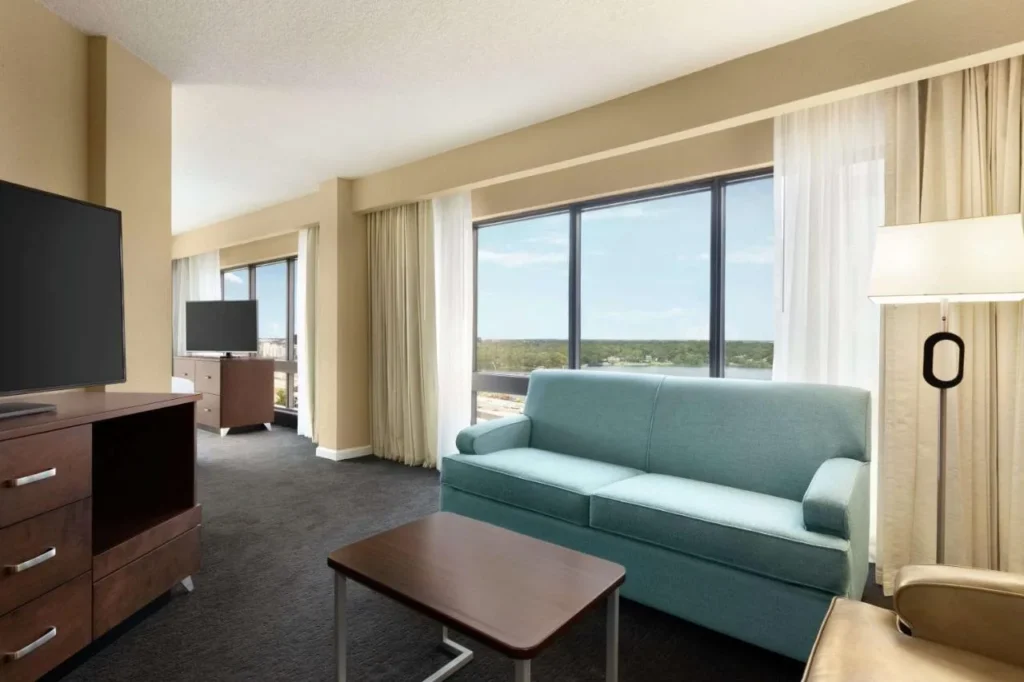 Suite sitting area with teal sofa and wide lake-view windows at DoubleTree Orlando Downtown