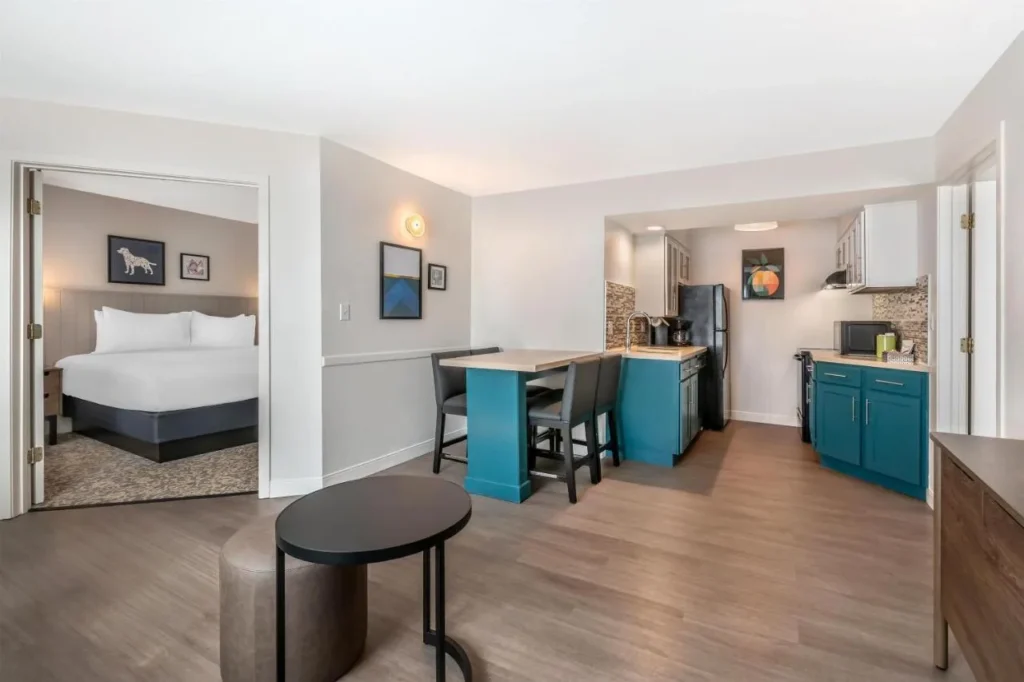 Suite con cocina de color verde azulado, mostrador de comedor y dormitorio con cama king en Sonesta ES Suites Lake Buena Vista