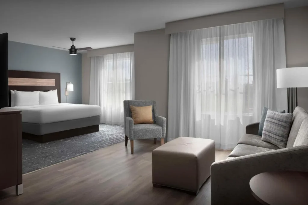 Suite con cama king size, sill&oacute;n, otomana y sof&aacute; en Homewood Suites by Hilton Orlando Airport
