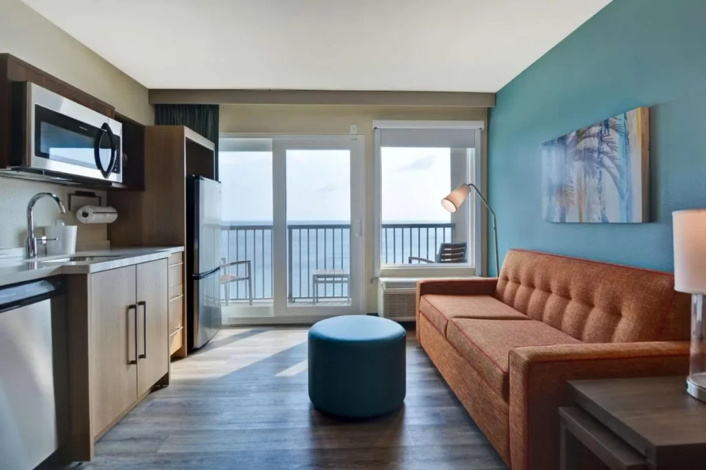 Suite con cocina, sofá y balcón con vista al mar en Home2 Suites Ormond Beach Oceanfront