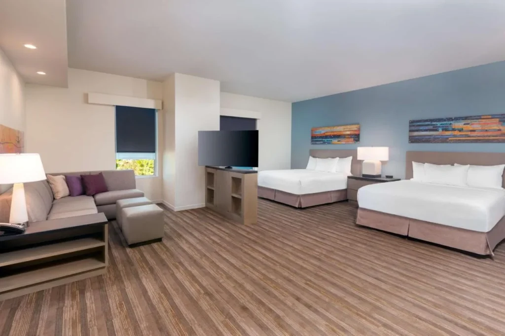 Suite with two queen beds, sectional sofa and wood-look floor at Hyatt House Orlando Airport