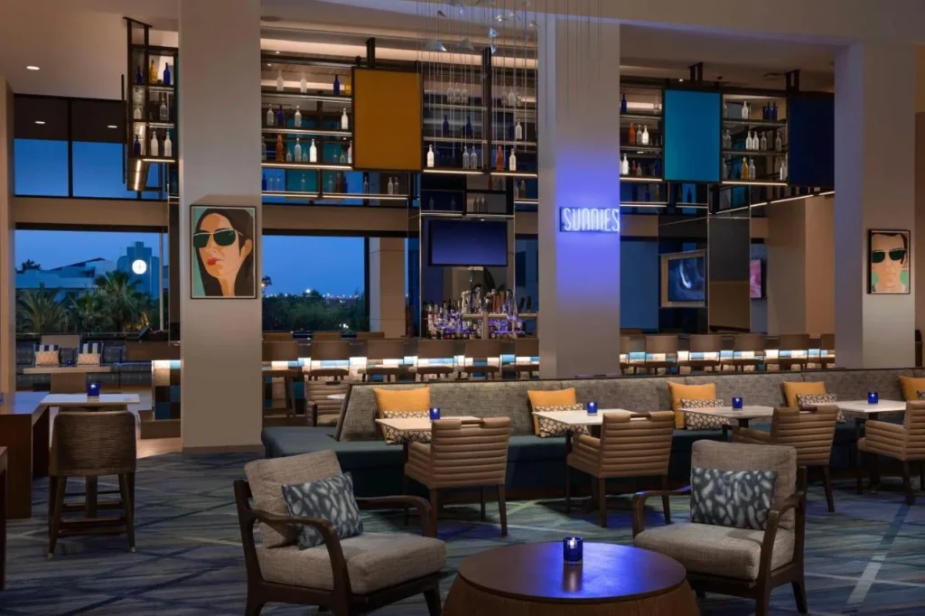 Sala de estar en el vest&iacute;bulo Sunnis con un bar retroiluminado y asientos para banquetes en el Hilton Orlando Buena Vista Palace