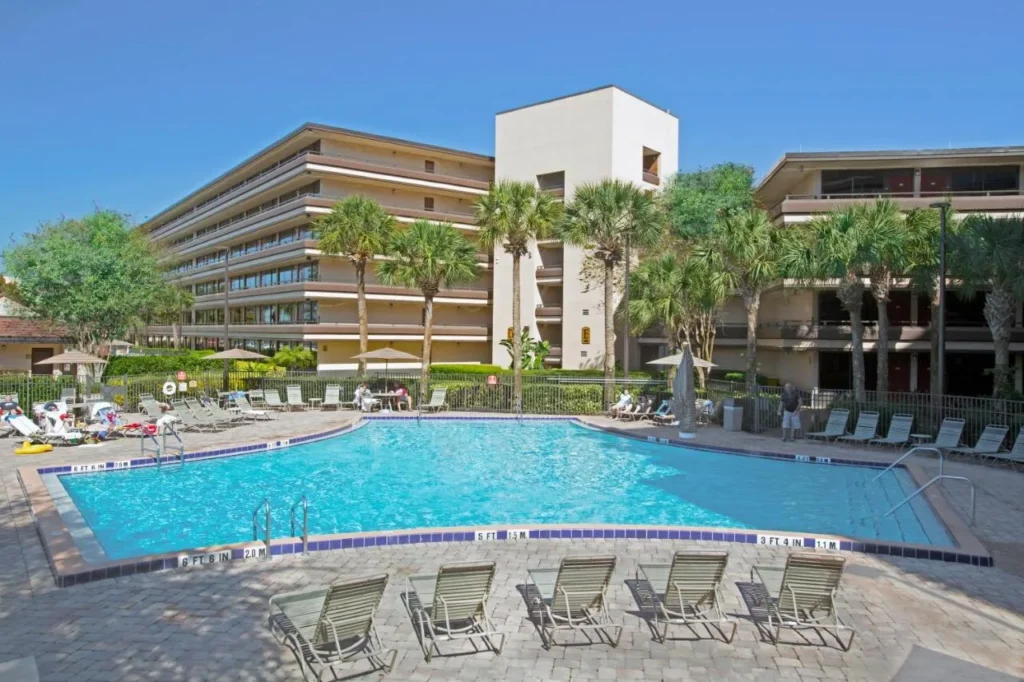 Sunny outdoor pool with loungers in front of the mid-rise guest buildings of Rosen Inn at Pointe Orlando