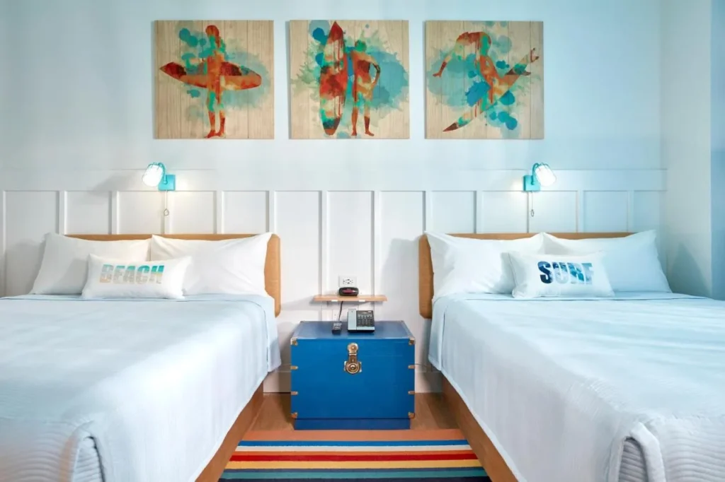 Habitación de huéspedes con dos camas y un baúl de almacenamiento azul en Universal's Surfside Inn