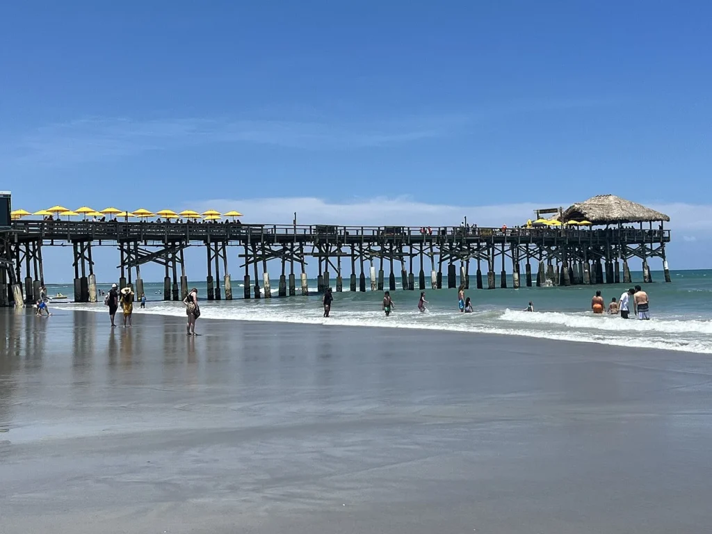 Swimmers in the surf beside the Cocoa Beach Pier with its yellow umbrellas and thatched-roof end