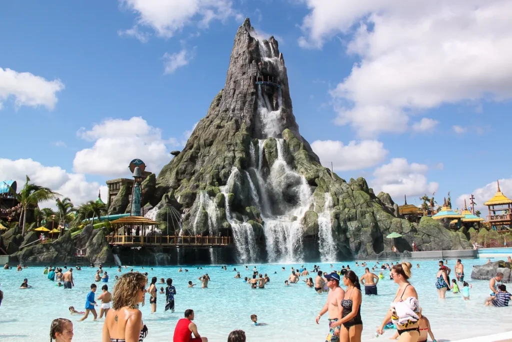 Nadadores en la piscina de olas debajo del volcán Krakatau y sus cascadas en Universal Volcano Bay