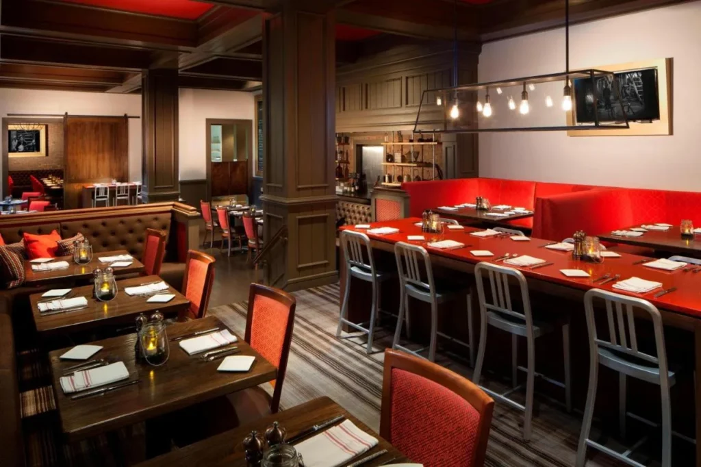 Comedor estilo taberna con banquetes rojos y mesas de madera en el Marriott Orlando Airport Lakeside