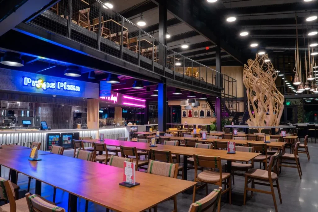 The Landing Food Hall with communal tables and a neon pizza sign at Evermore Orlando Resort