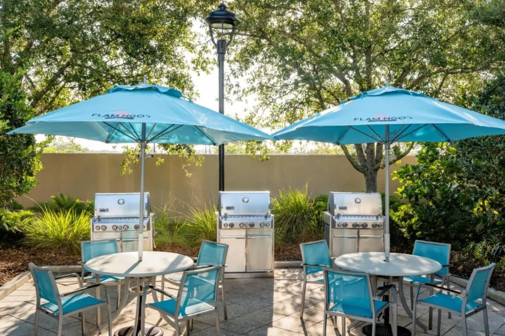 Tres parrillas de gas y mesas de patio bajo sombrillas azules en SpringHill Suites Flamingo Crossings
