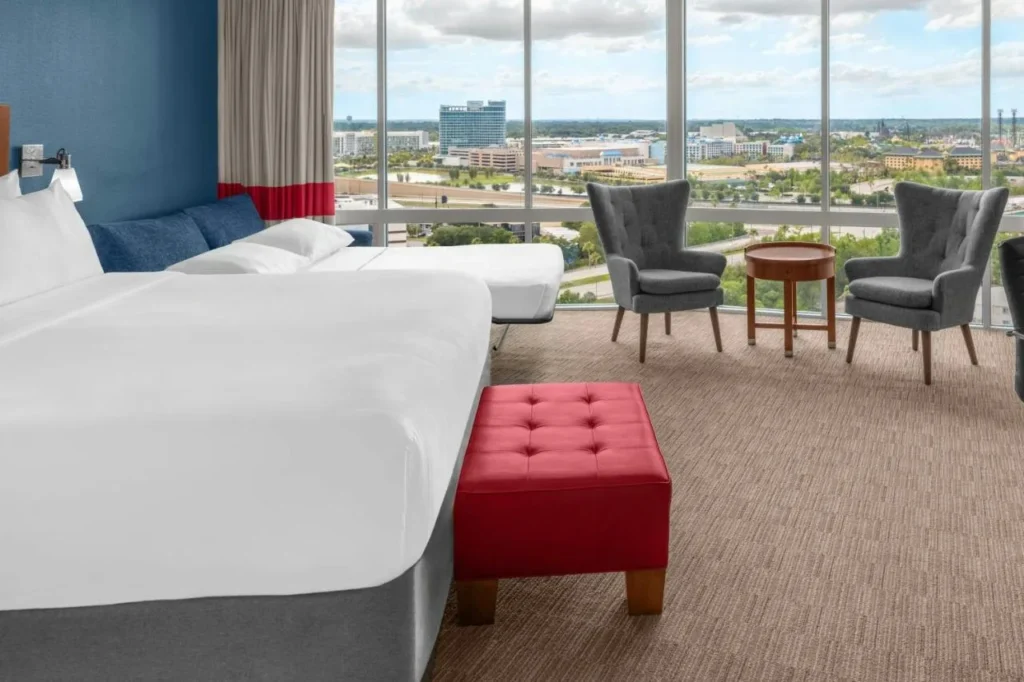 Habitación en planta alta con una cama grande, sofá cama abierto y ventanas de piso a techo en Four Points I-Drive