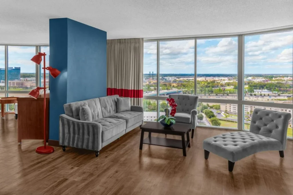 Sala de estar en la suite de la planta superior con sofá gris, tumbonas y ventanas del piso al techo en Four Points I-Drive