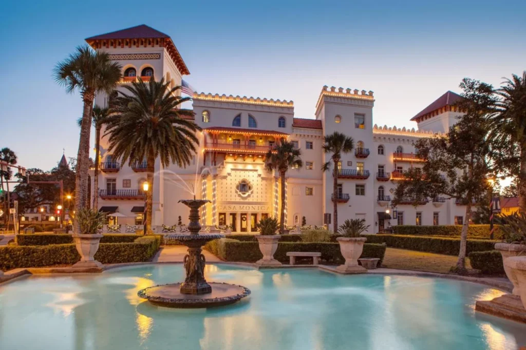 Towers and lit facade of Casa Monica Resort & Spa at dusk behind a fountain