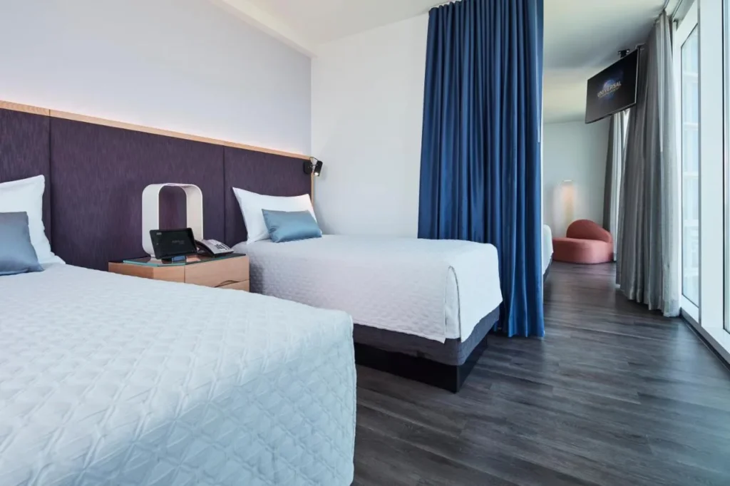 Twin-bed kids' area beside a blue divider curtain in a Kids' Suite at Universal Aventura Hotel