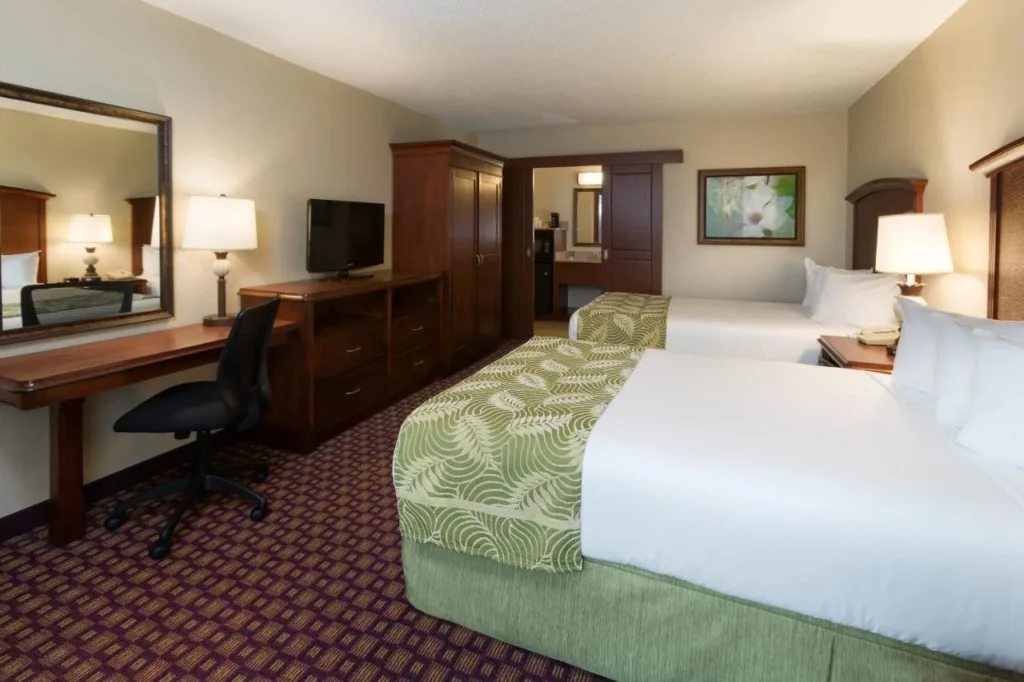 Habitación de dos camas con escritorio de madera y TV de pantalla plana en Rosen Inn at Pointe Orlando