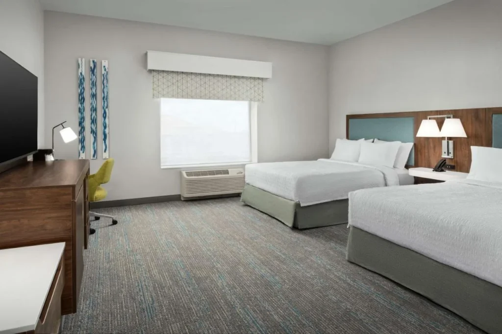 Habitaci&oacute;n de dos camas con escritorio, silla amarilla y ventana en Hampton Inn Orlando Southeast Nona