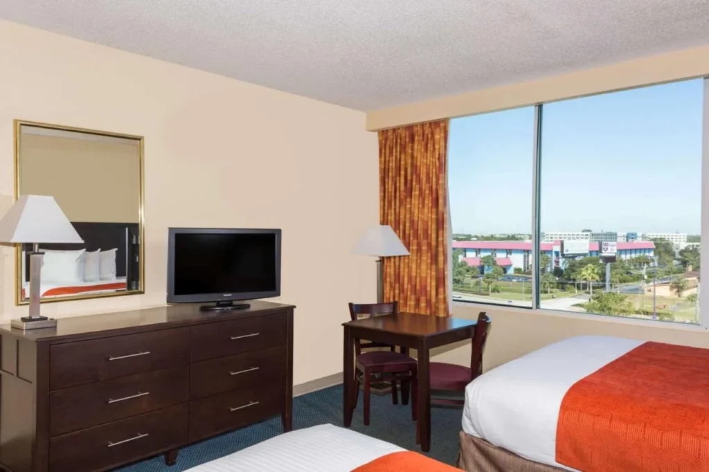 Two-bed room with dresser, small table and large window view at Ramada Kissimmee Gateway