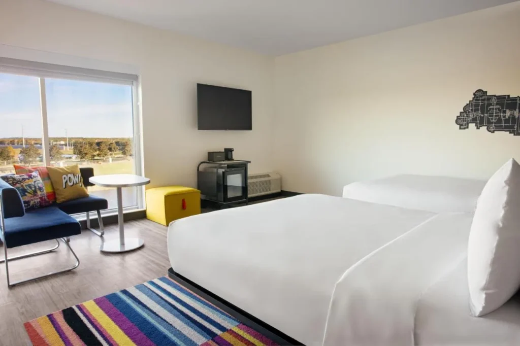 Habitaci&oacute;n de dos camas con alfombra a rayas, sof&aacute; azul y ventana grande en Aloft Orlando Lake Nona