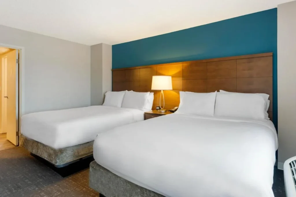 Two beds below a wood headboard wall in a suite bedroom at Staybridge Suites Royale Parc