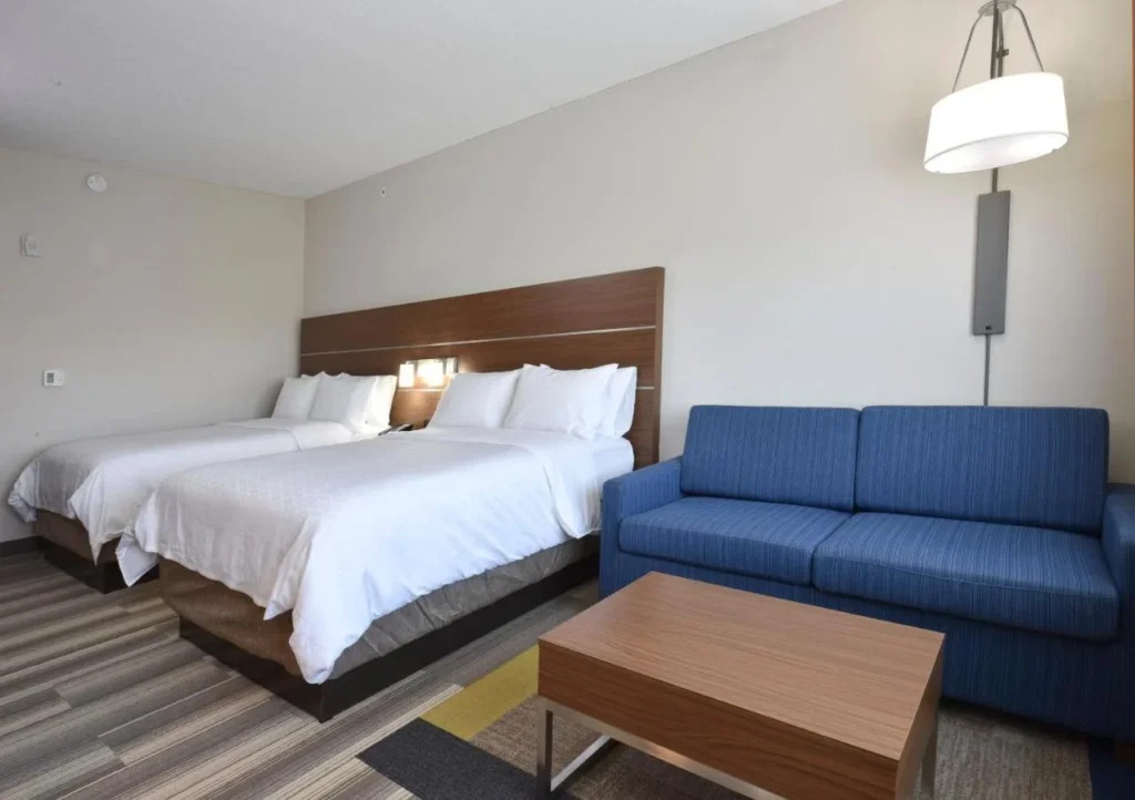 Dos camas, sof&aacute; azul y mesa de centro en una habitaci&oacute;n en Holiday Inn Express Orlando Southeast