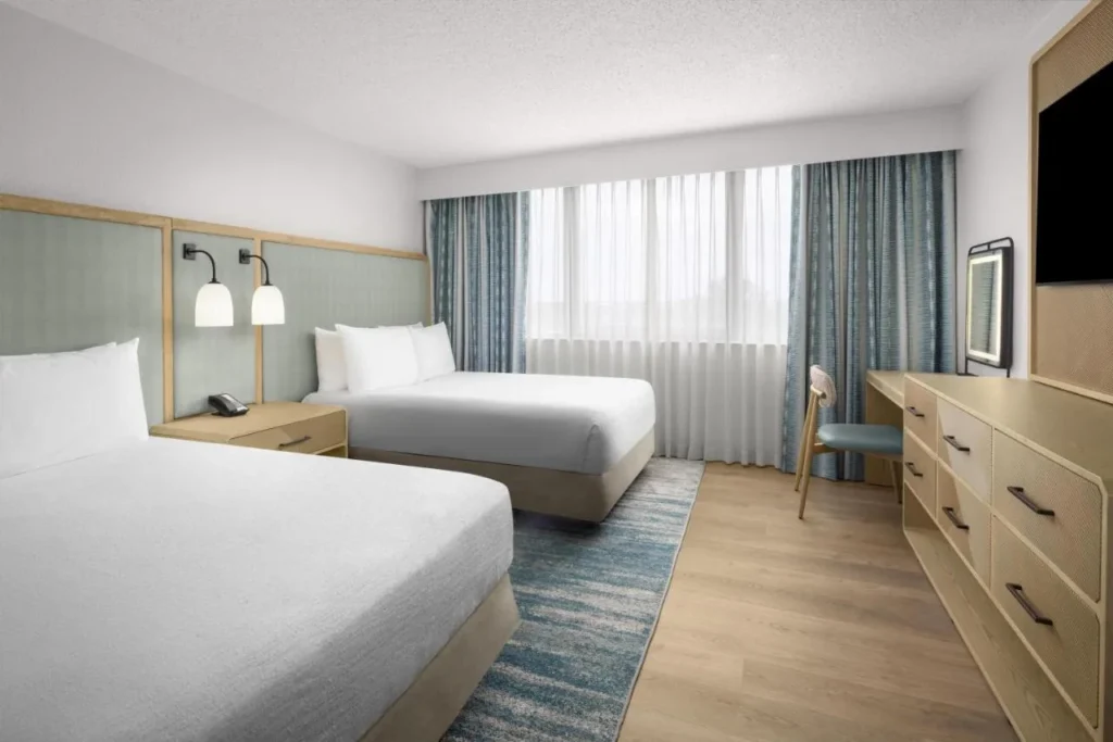 Dos camas, tocador, escritorio y TV de pared en un dormitorio suite en Embassy Suites ICON Park