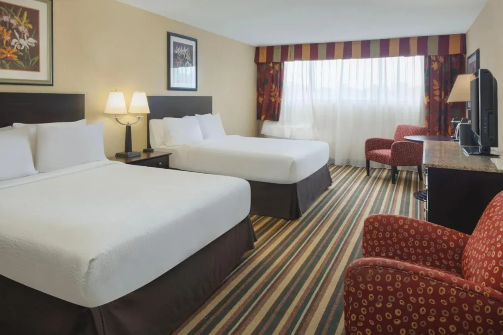 Dos camas, sillones rojos y una amplia ventana en Holiday Inn & Suites Orlando SW