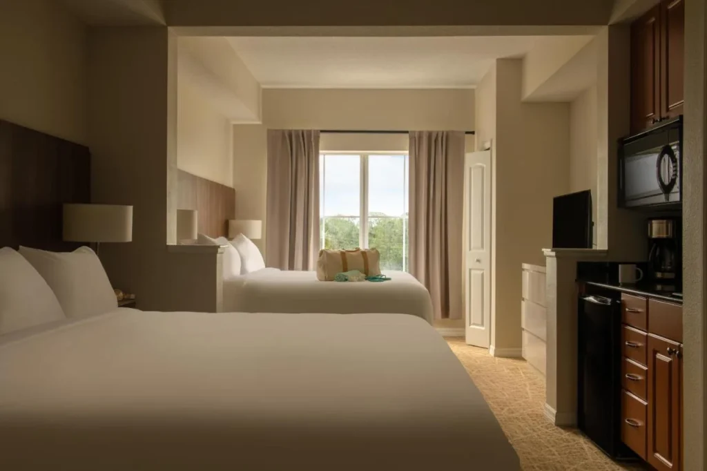 Dos camas, TV y cocineta con microondas en una suite en The Point Hotel & Suites