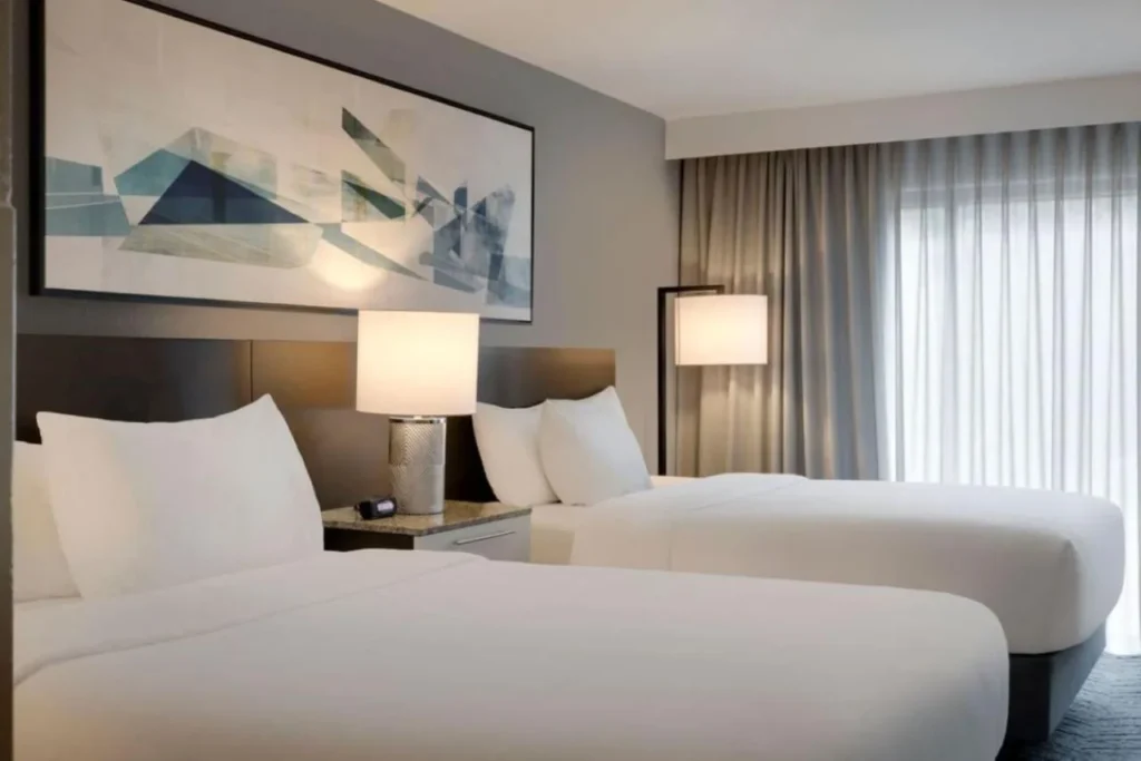 Dos camas con sábanas blancas, una lámpara de noche y obras de arte abstractas en Delta Hotels Orlando Celebration