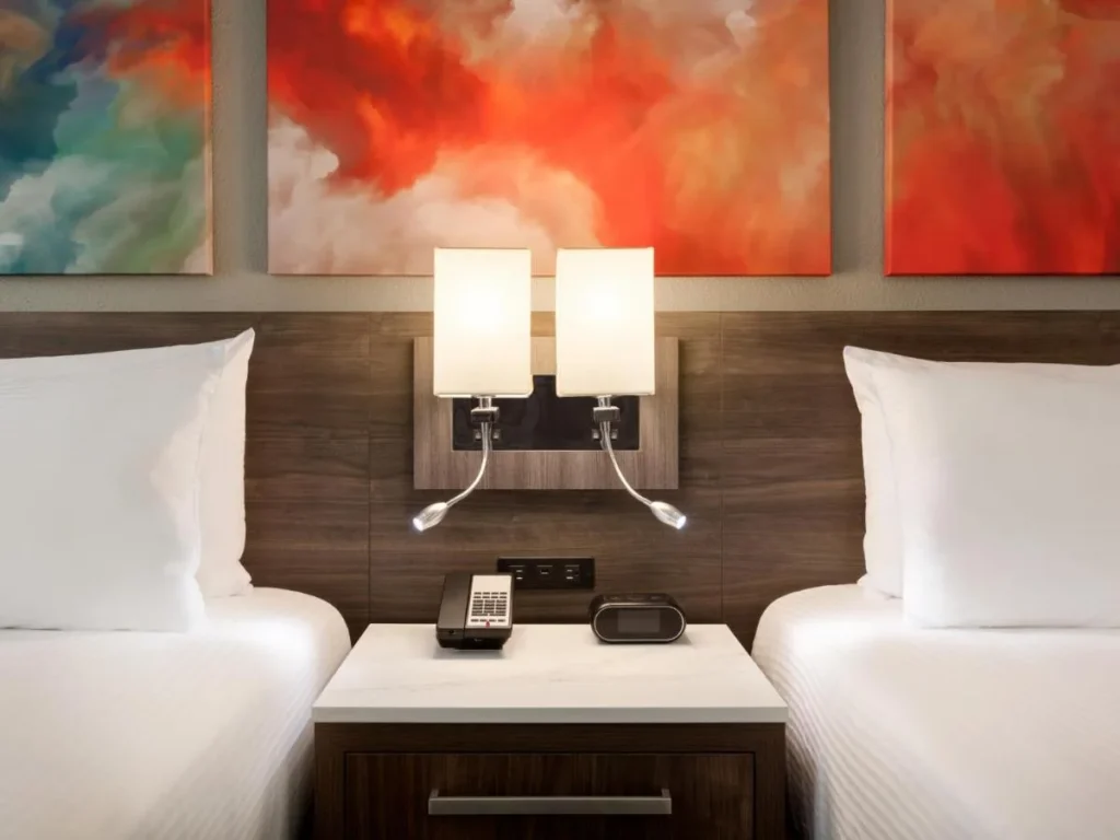 Two beds with white linens and twin reading lamps under abstract art at Buena Vista Suites