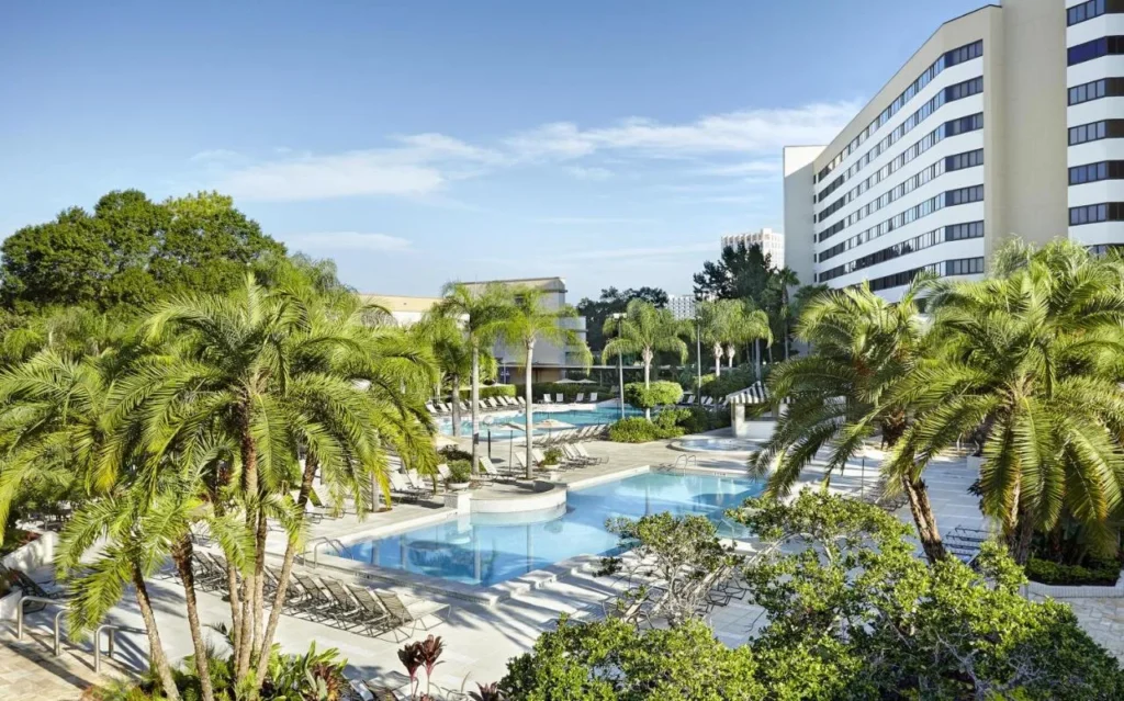 Dos piscinas rodeadas de palmeras junto a la torre blanca del Hilton Orlando Lake Buena Vista
