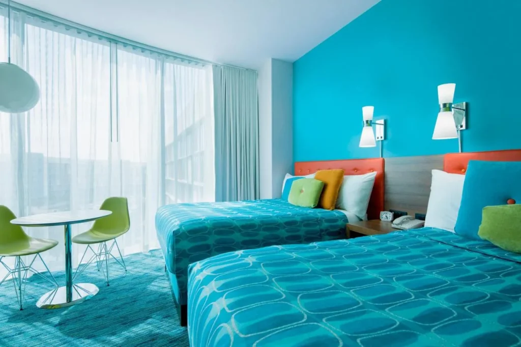 Dos camas queen con l&aacute;mparas de pared retro y una mesa de bistro en Cabana Bay Beach Resort