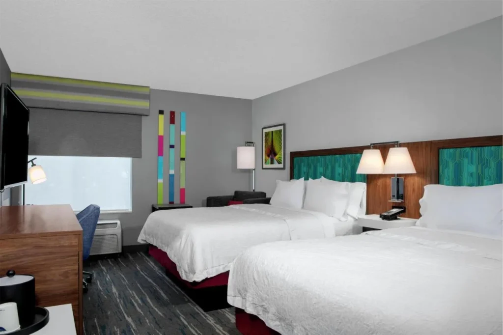 Two queen beds with teal headboards, desk and armchair at Hampton Inn Orlando/Lake Buena Vista