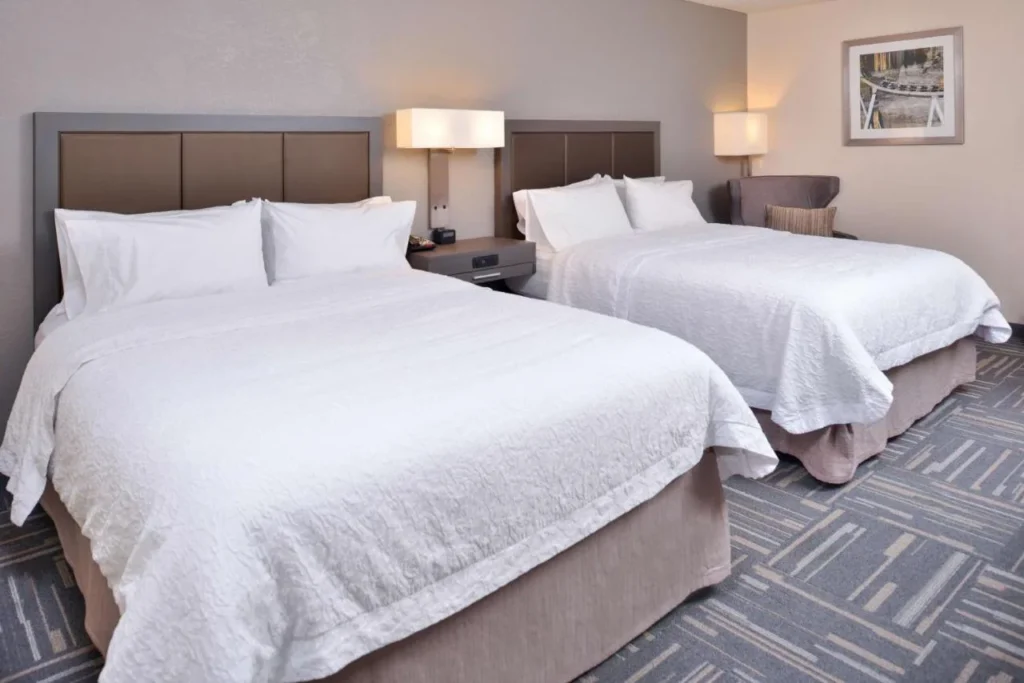 Two queen beds with white bedding and bedside lamps at Hampton Inn Closest to Universal