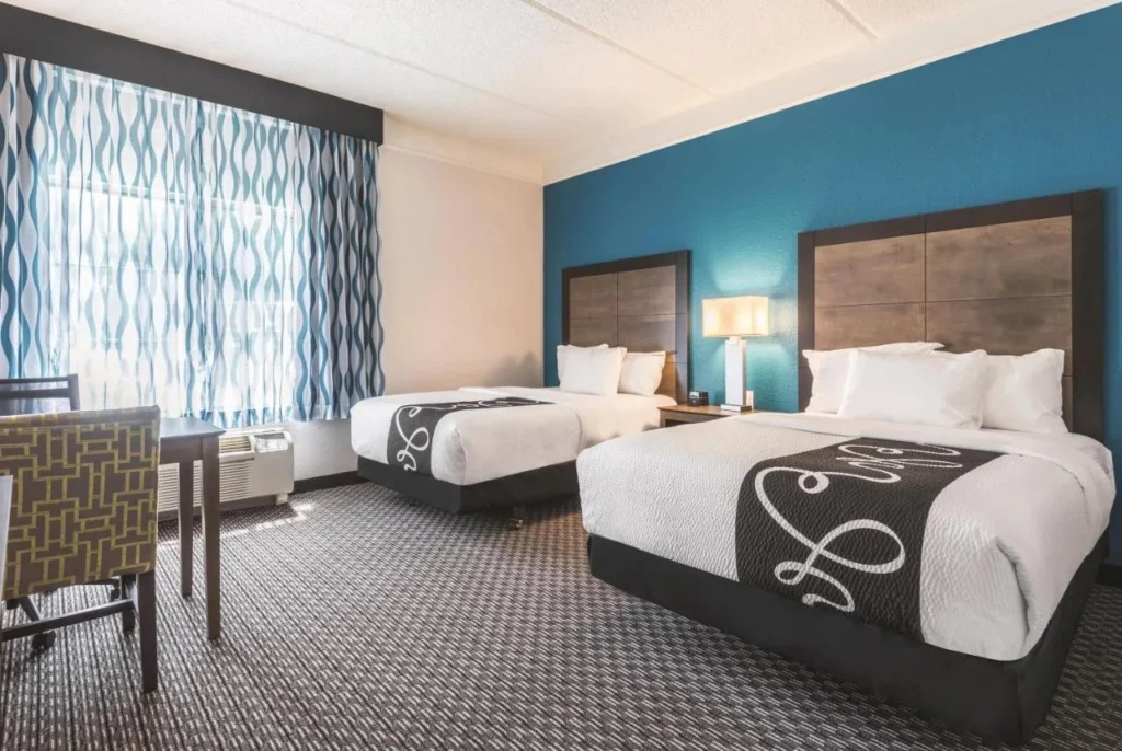 Habitación de dos camas queen con una pared de acento azul y escritorio en La Quinta Orlando Lake Mary