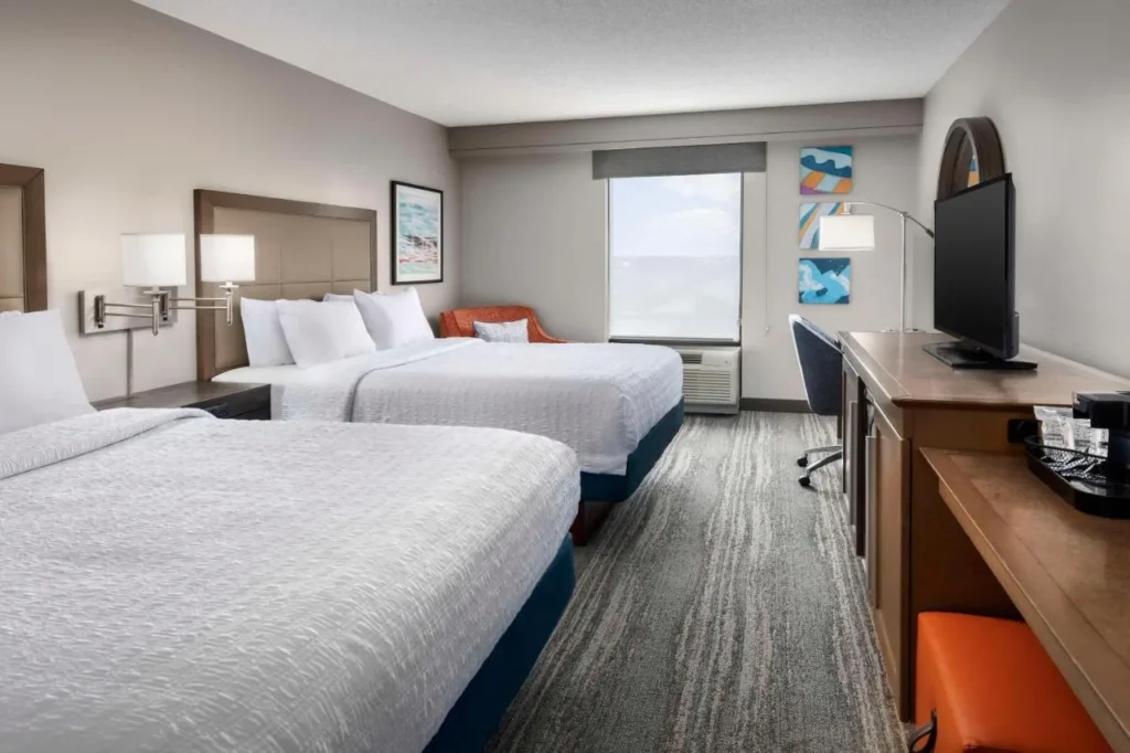 Habitación de dos camas queen con escritorio, sillón y TV en Hampton Inn & Suites Lake Mary