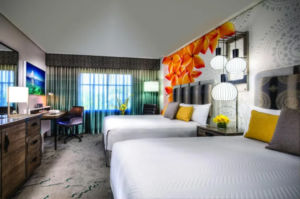 Two-queen guest room with an orange flower mural and a desk at Loews Royal Pacific Resort