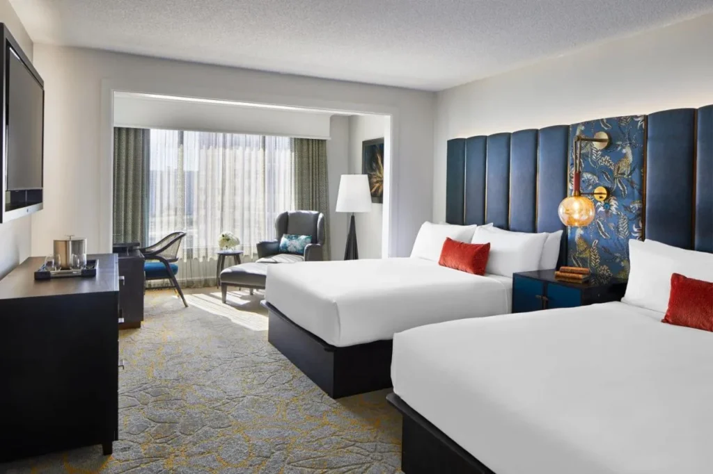 Two-queen guest room with blue upholstered headboards and an armchair by the window at Hotel Beauden