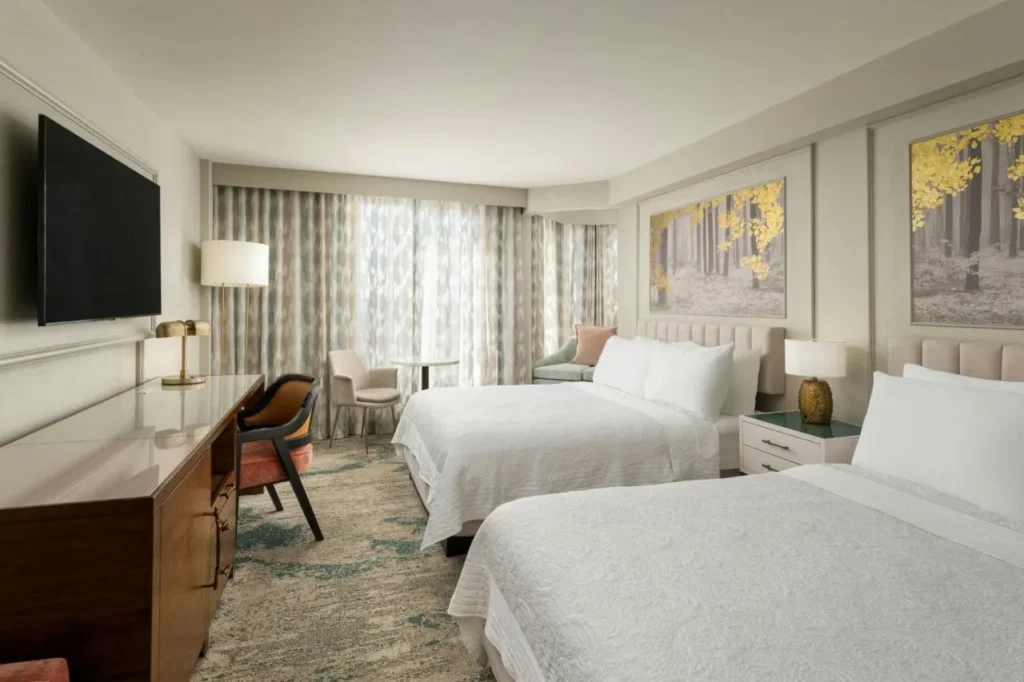 Two-queen guest room with gold forest artwork and a long desk at Castle Hotel Orlando