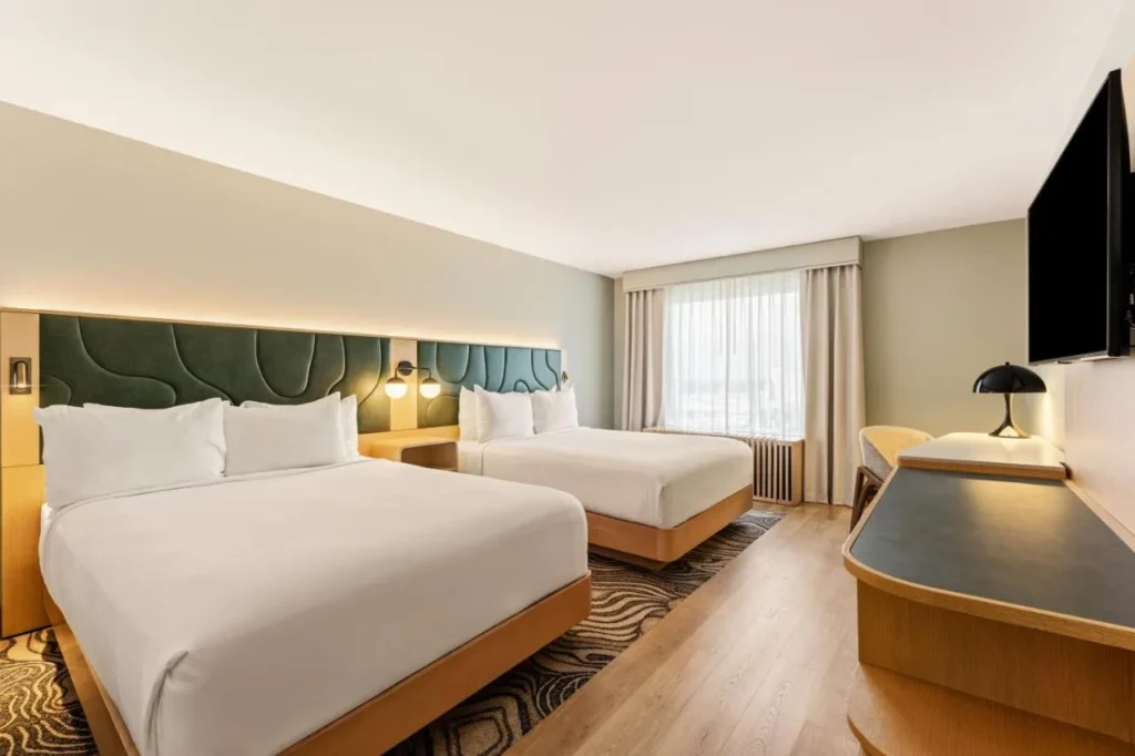Two-queen guest room with padded green headboards and wood floors at Rosen Plaza Hotel